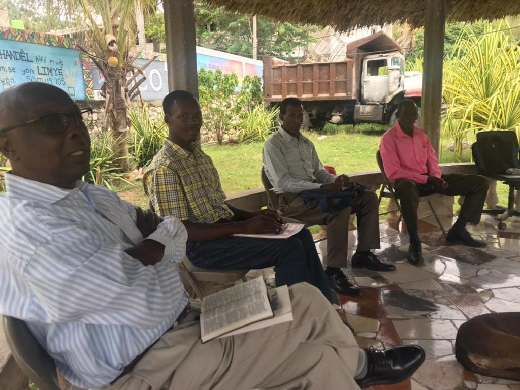 Pastoral retreat with four men sitting in shaded outdoor structure